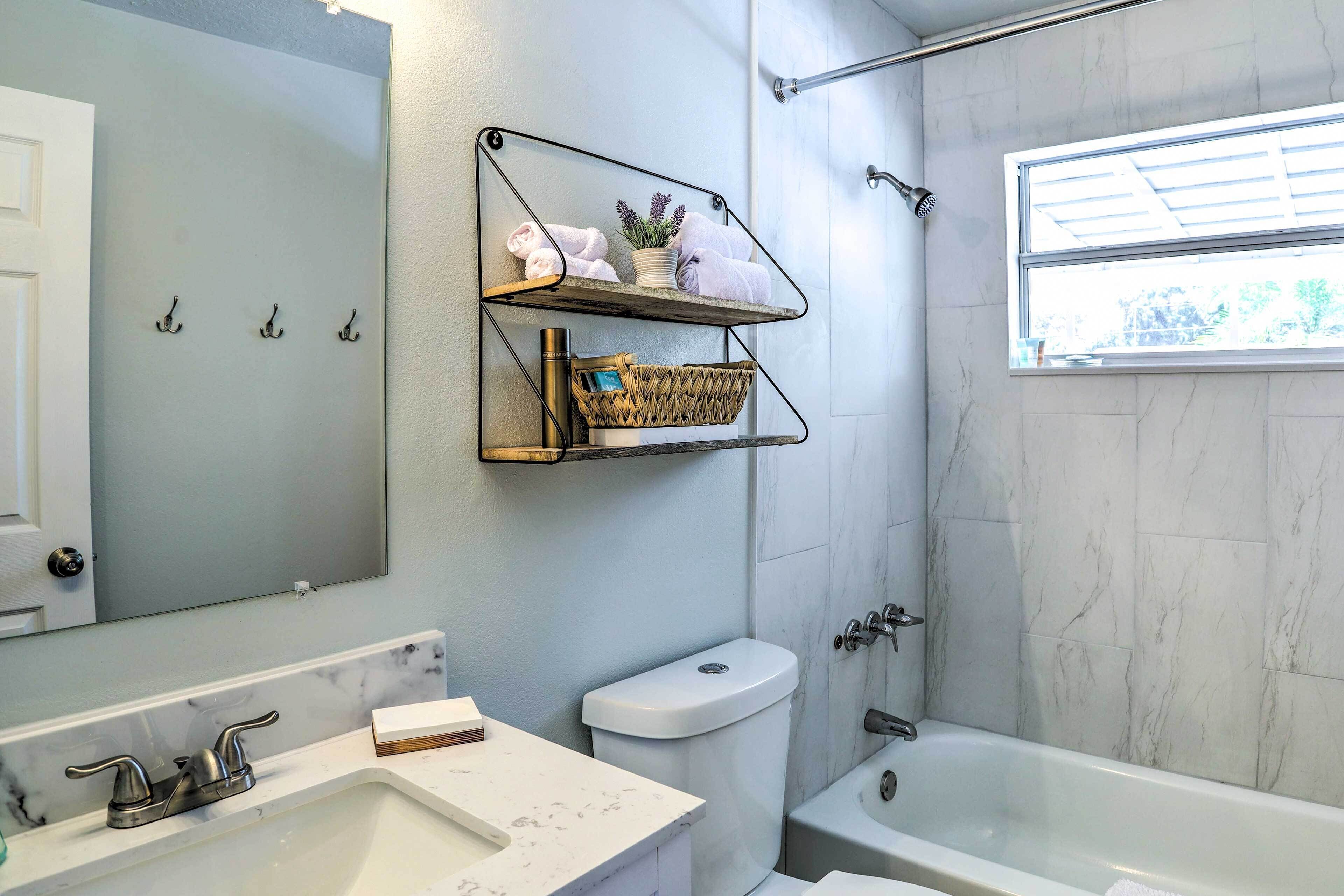 A bathroom with a white sink, a toilet, a bathtub, and a shower. There are two metal shelves mounted on the wall, one holding towels and the other a basket.
