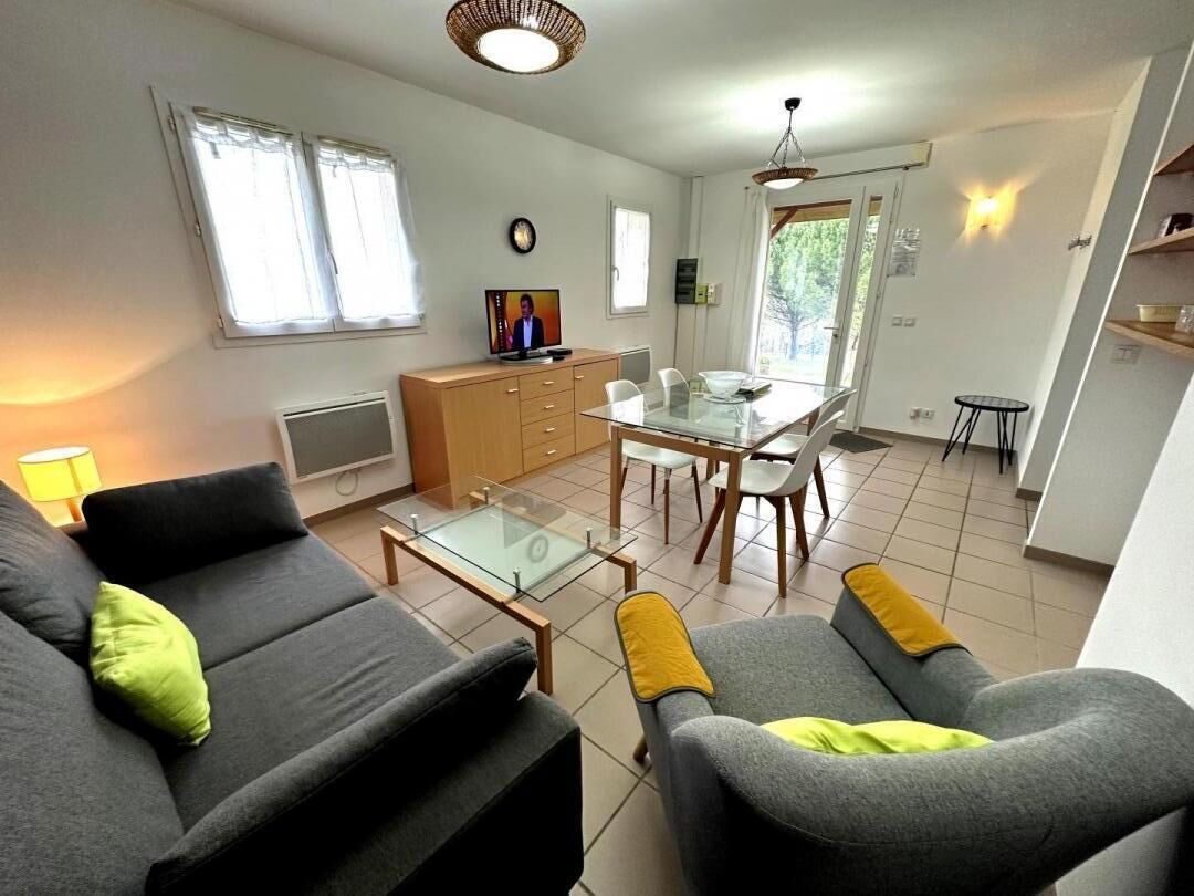Ein modernes Wohnzimmer mit einer Couch, Sesseln, einem Glastisch und einem Essbereich mit Tisch und Stühlen.