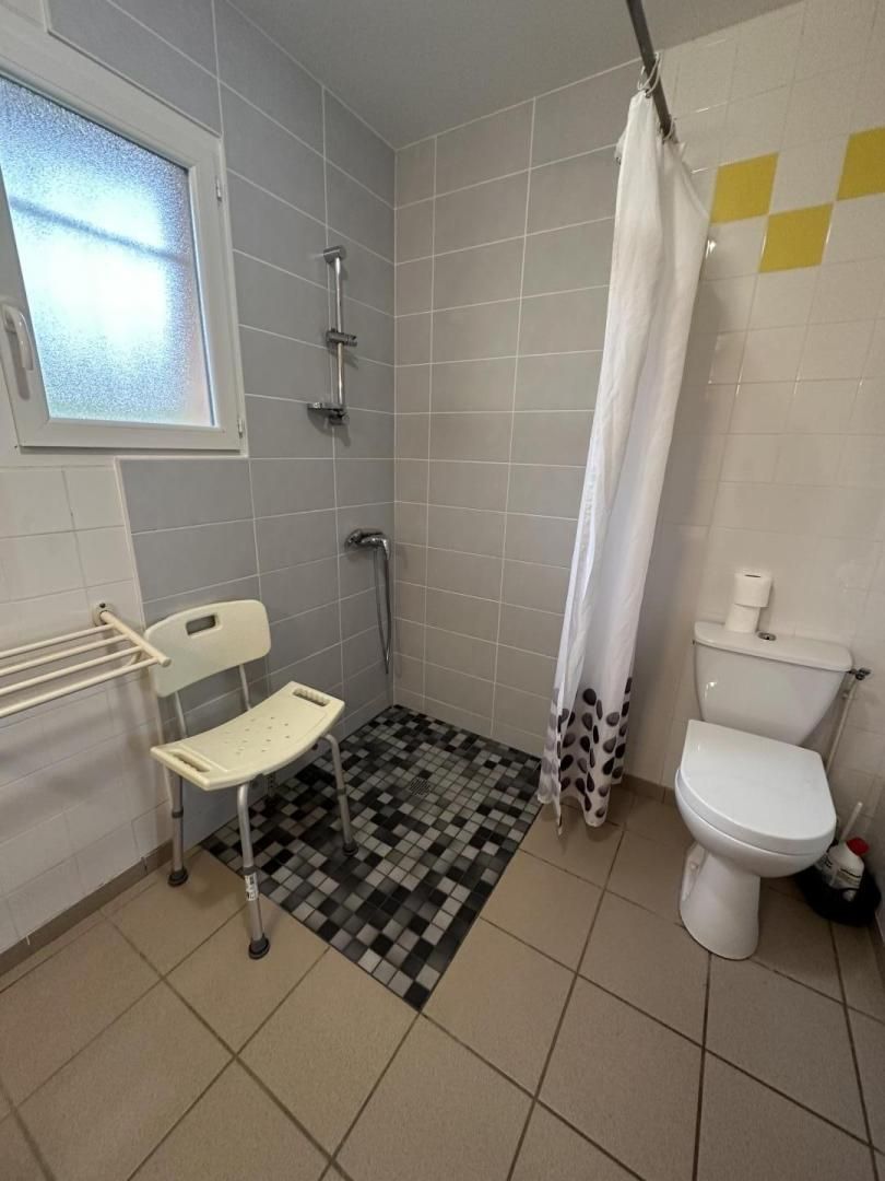 Baño pequeño con ducha, inodoro y una silla.