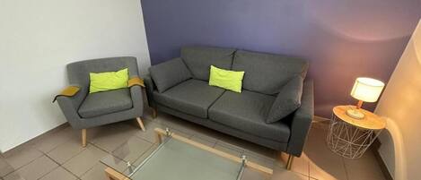 A living room with a grey sofa, a smaller armchair, and a glass coffee table.