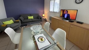 Ein modernes Wohnzimmer mit einem Glastisch, einer Couch, einem Fernseher und einer Uhr an der Wand.