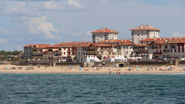 Ein Küstenhotel mit mehreren Gebäuden, ein Strand im Vordergrund und ein klarer Himmel.