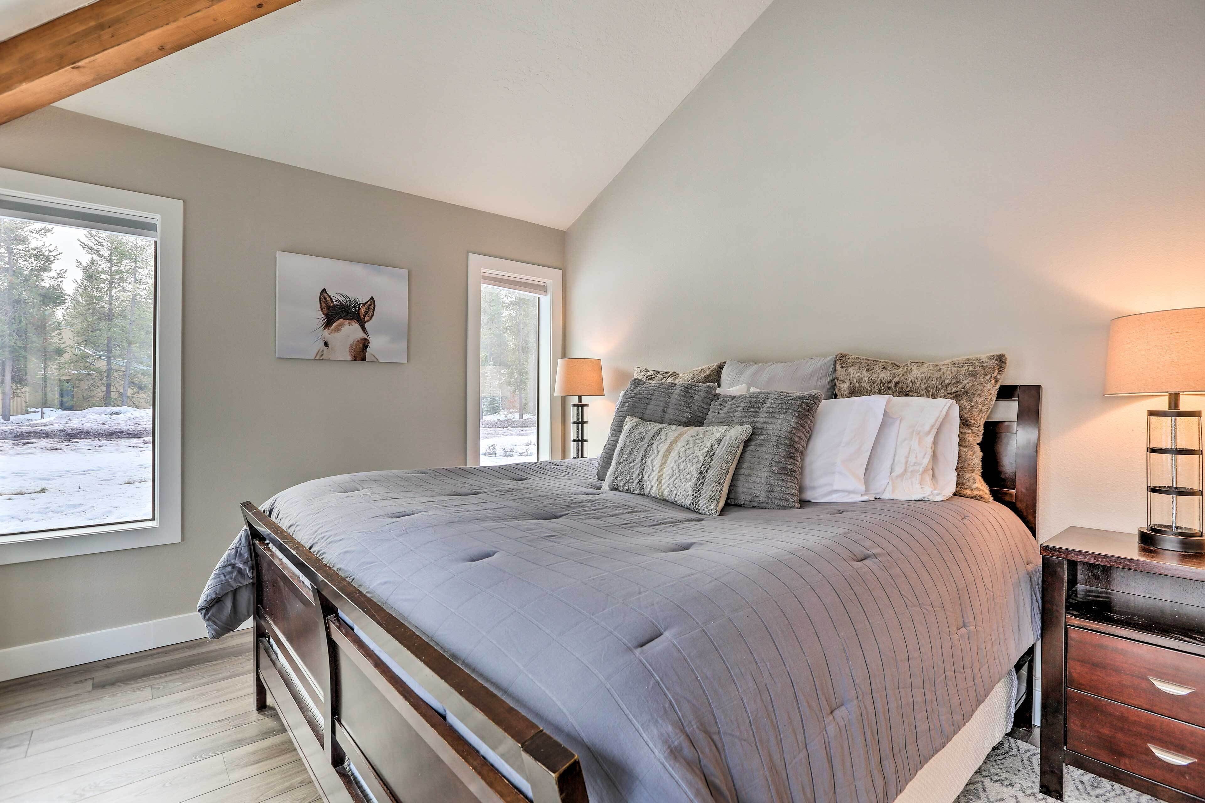 A bedroom with a large bed, two bedside lamps, a nightstand, and a window with a view of trees.