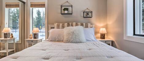 A bedroom with a large bed, two bedside tables with lamps, a fluffy pillow, and two wall-mounted picture frames.