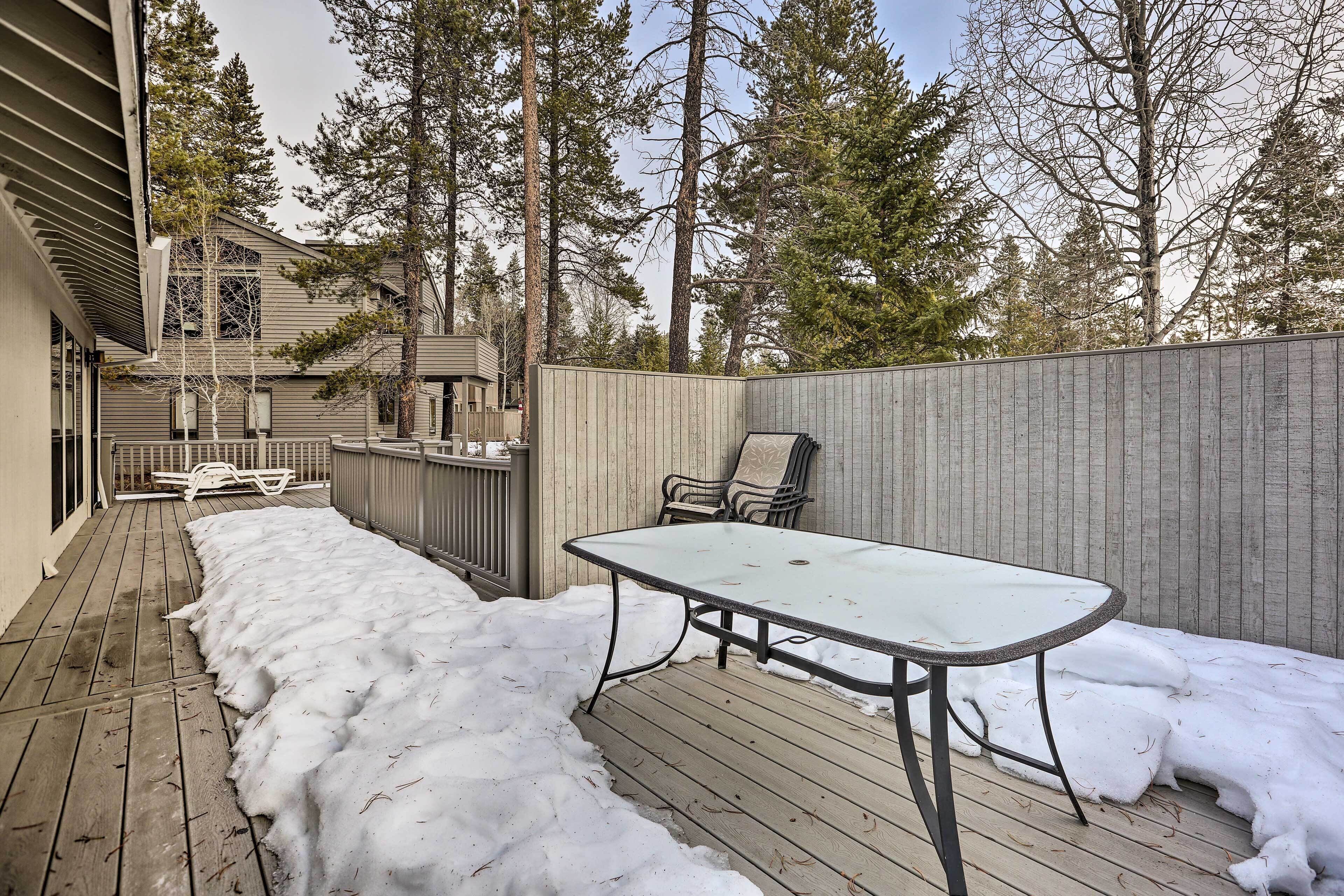 A wooden deck with a metal table and chairs, surrounded by a wooden fence and tall trees.