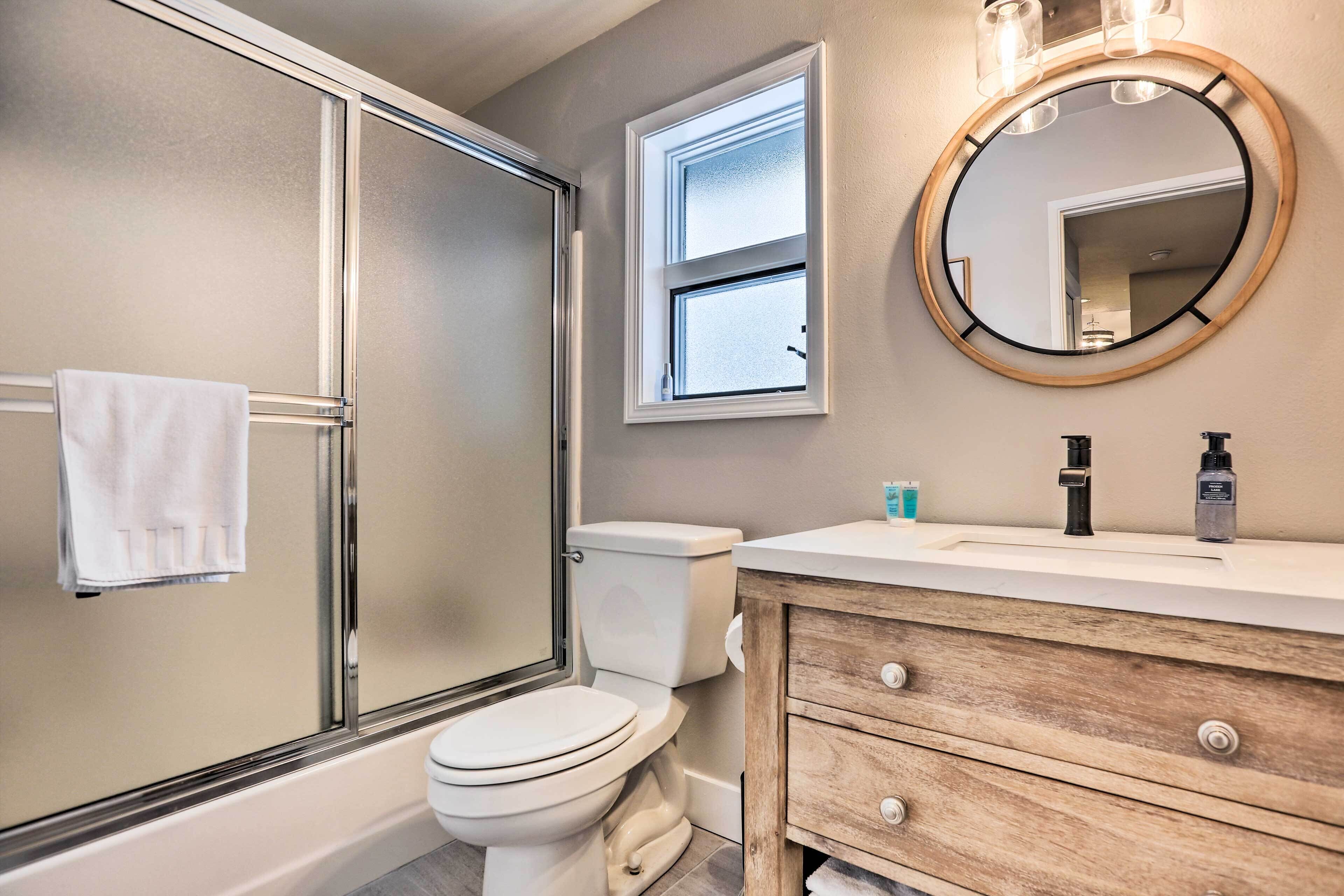 Een moderne badkamer met een douchecabine van glas, een wit toilet, een houten wastafelmeubel met lades en een ronde spiegel boven de wastafel.