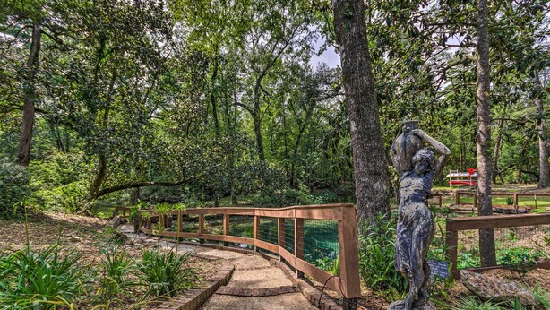 Eine hölzerne Brücke in einem bewaldeten Gebiet mit einer Statue einer Frau auf einem Sockel.
