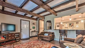 Ein Wohnzimmer mit Fernseher, Sofas, Teppich und einer Küchenzeile mit Spüle und Spiegel.