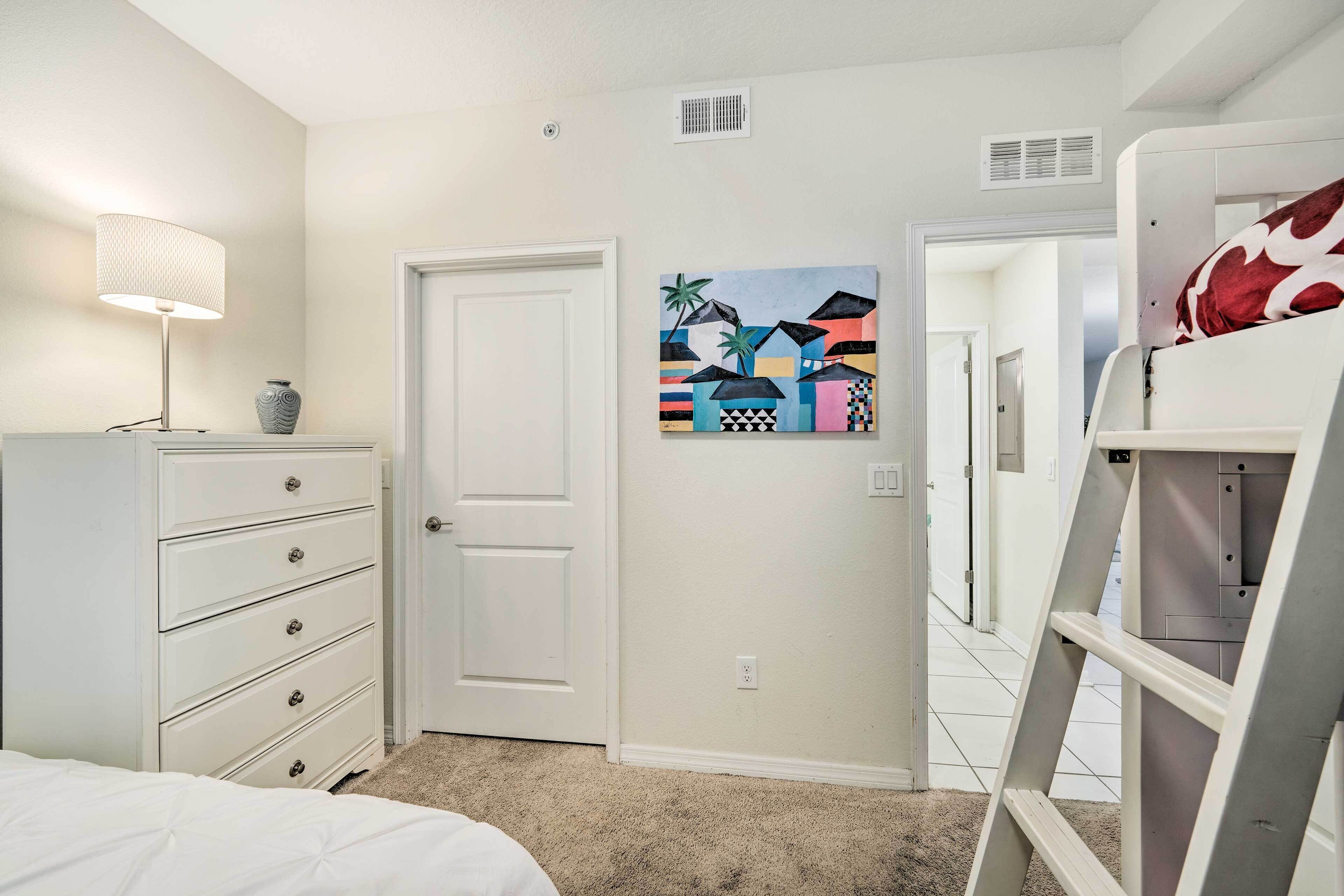 A bedroom with a white dresser, a bed, a painting on the wall, and a ladder.
