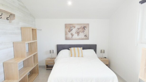 Une chambre à coucher avec un lit, une œuvre d’art représentant une carte du monde, des étagères en bois et deux tables de chevet avec des lampes.