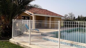Une piscine entourée d’une clôture blanche, avec un espace abrité et un palmier.