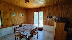 A wooden-paneled room with a dining table and chairs, a ceiling fan, and a kitchen area.