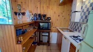 A compact kitchen with wooden walls, a microwave, a sink, and a stove.