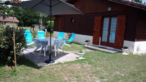 An outdoor patio with a table and chairs, a wooden building with a door, and a small garden area.