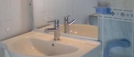 Ein Badezimmer mit weißem Waschtisch, Waschbecken, Spiegel und Duschbereich.