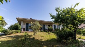 A two-story house with a tiled roof, a front porch, and a small garden with a tree and shrubs.