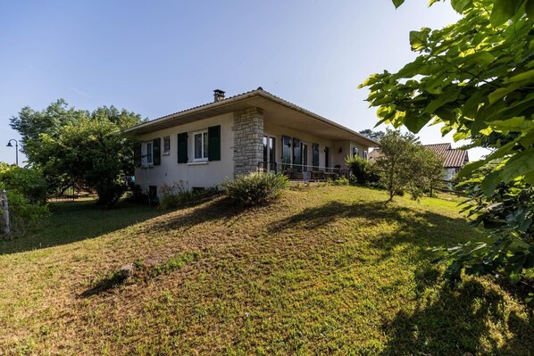 A single-story house with a stone facade, green shutters, and a sloped roof.