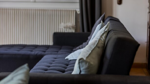 A modern bedroom with a dark-colored sofa bed, a radiator, and a window with curtains.