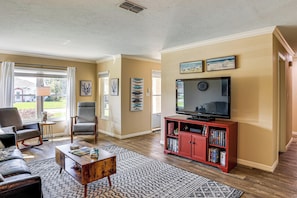 A living room with a sofa, chairs, a coffee table, a TV, and a bookshelf.