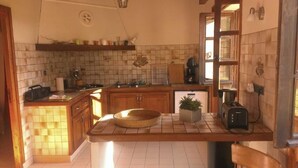 A kitchen with wooden cabinets, a tiled backsplash, a central island with a basket, a toaster, and a potted plant.