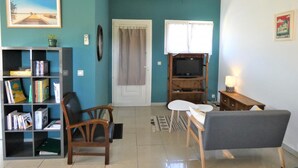 A living room with teal walls, a bookshelf, a TV, and a dining area. - Les Palombières - SOUSTONS (SOUSTONS)