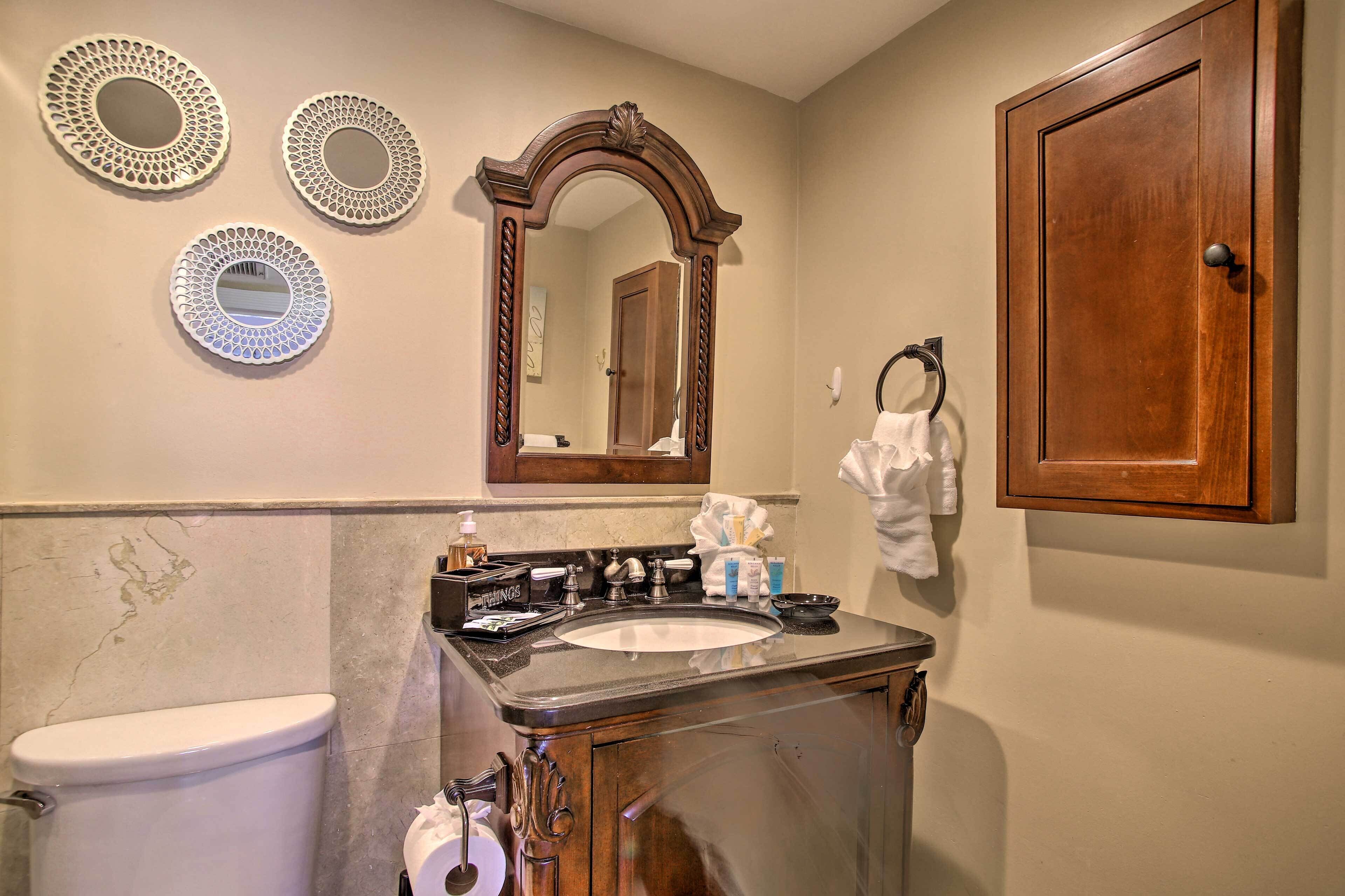 A bathroom with a sink, mirror, and toilet. There are three decorative mirrors on the wall.
