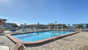 A rectangular swimming pool with a brick border, surrounded by lounge chairs and umbrellas, with a clear blue sky above. - 'the Palms' Cocoa Beach Condo: Walk to Beach! (Cocoa Beach)