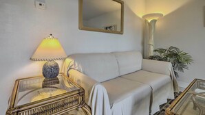 A room with a white sofa, a glass table with a decorative item, a lamp, and a mirror on the wall. - 'the Palms' Cocoa Beach Condo: Walk to Beach! (Cocoa Beach)