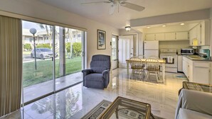 A spacious living room with a large window, a ceiling fan, and a dining area with a table and chairs. - 'the Palms' Cocoa Beach Condo: Walk to Beach! (Cocoa Beach)