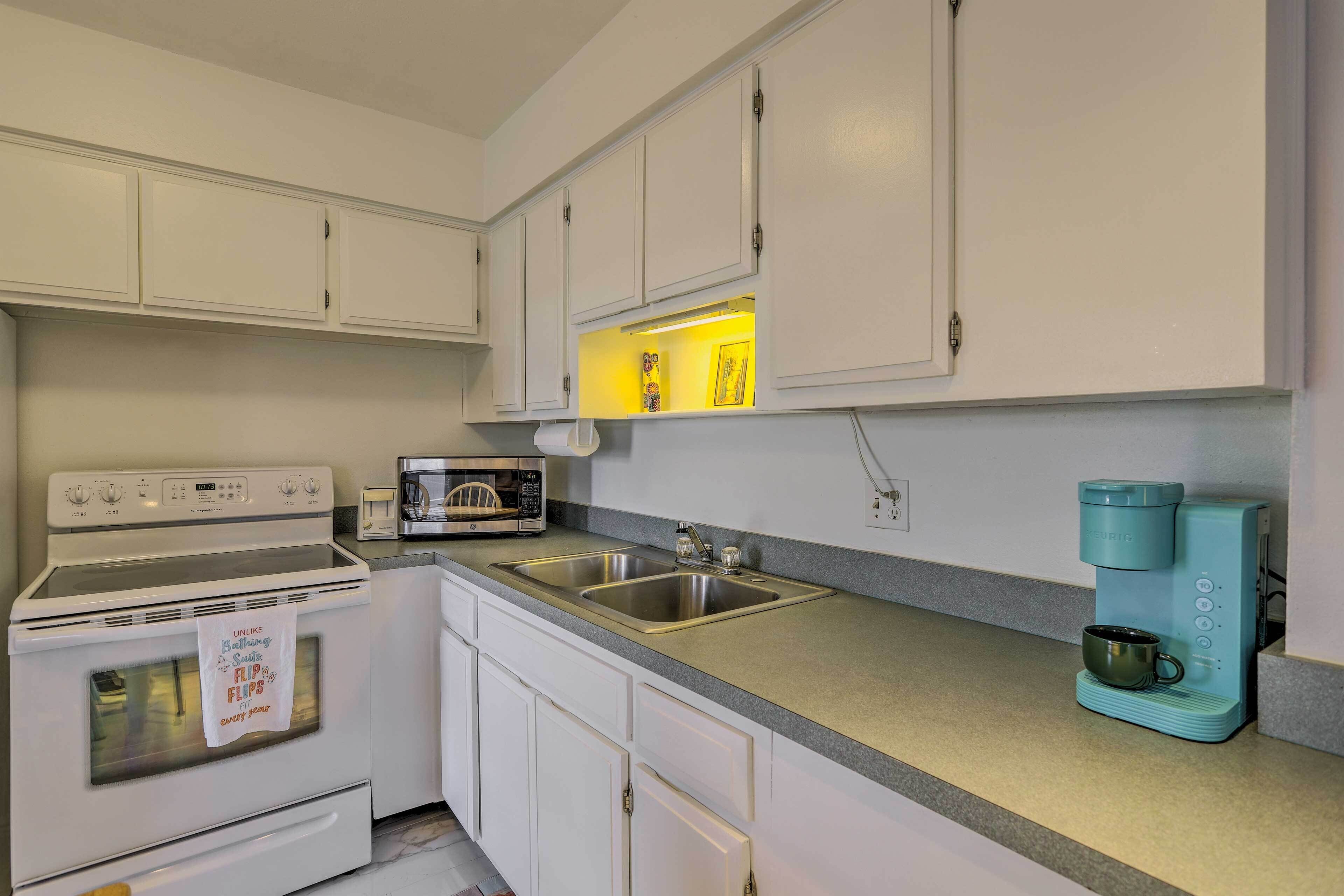 A kitchen with white cabinets, a stainless steel sink, a microwave, a stove, and a coffee maker.