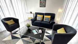 Ein modernes Wohnzimmer mit einer schwarzen Ledersofa, zwei Sesseln, einem Couchtisch und einem geometrischen Teppich.