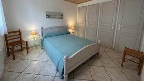 Un dormitorio con una cama, dos mesitas de noche con lámparas, una silla de madera, un armario y un banco.