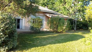 Una casa con techo de tejas, rodeada de un césped cuidado y diferentes arbustos.