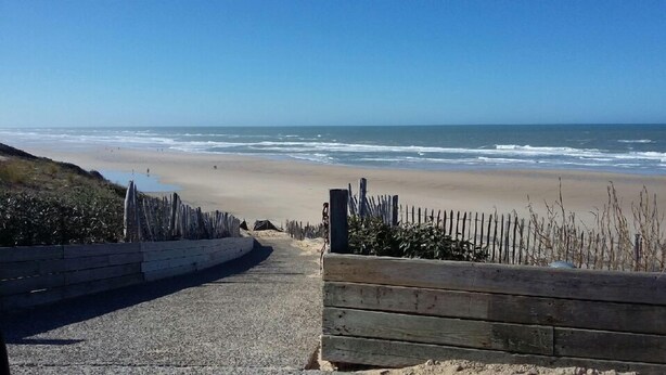 Un camino pavimentado que lleva a una playa, con una valla de madera y una barrera de hormigón.