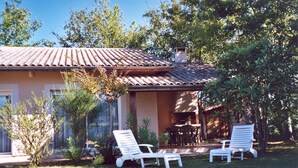 Una casa con techo de tejas, un patio con dos sillones blancos y una mesa pequeña.
