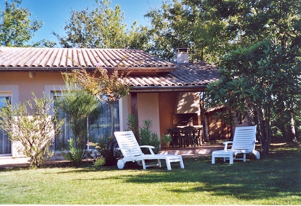 A house with a tiled roof, a patio with two white lounge chairs, and a small table.