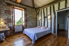 Un dormitorio con pared de piedra, vigas de madera, una cama, una ventana y un radiador.