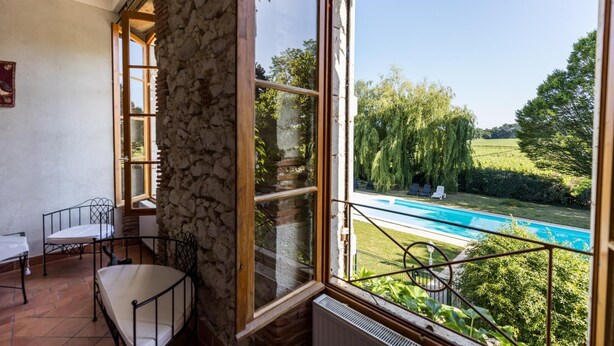 Une pièce avec un mur en pierre, une fenêtre donnant sur une piscine et un fauteuil.