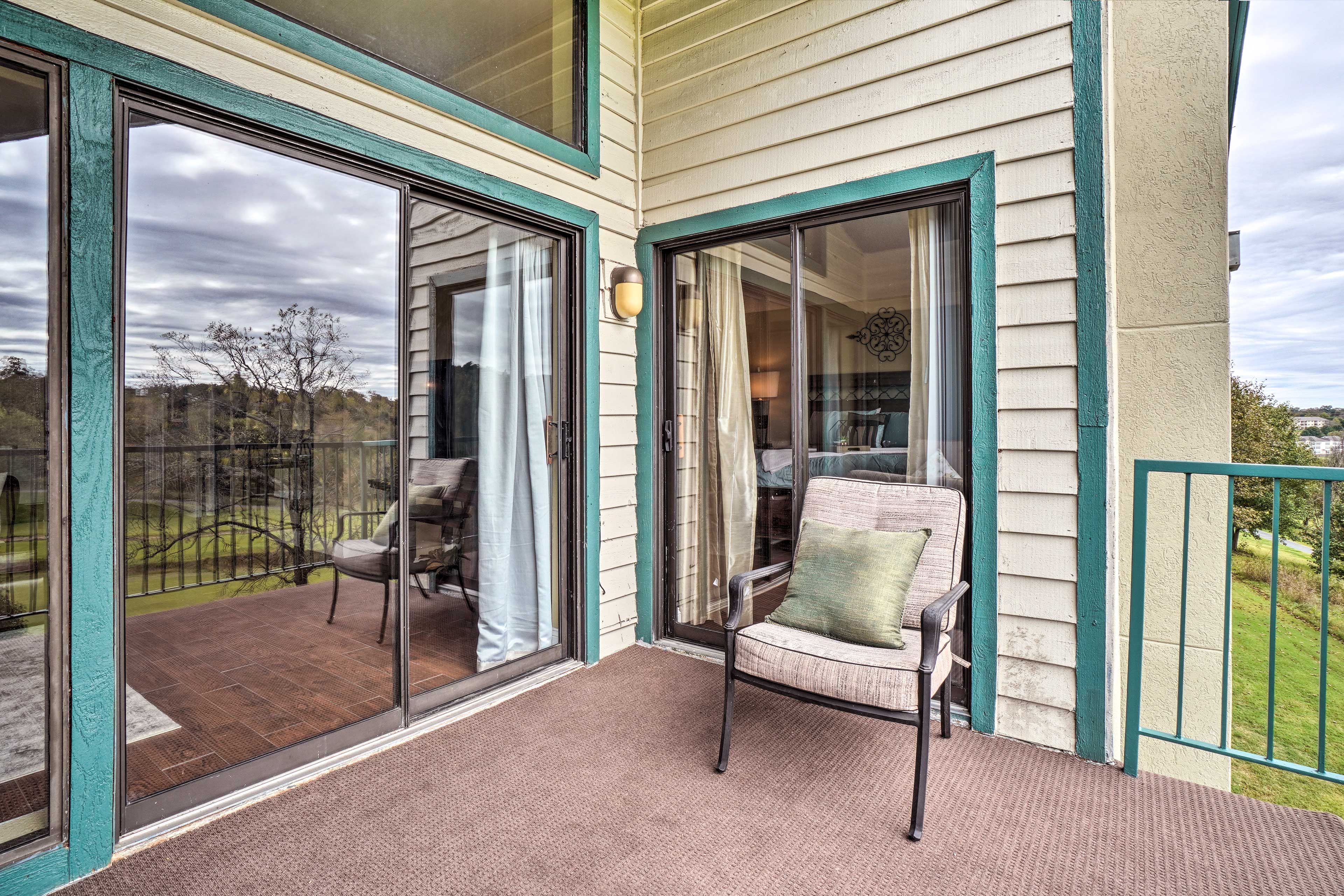 A covered patio with a chair and a table, large sliding glass doors, and a view of a grassy area.