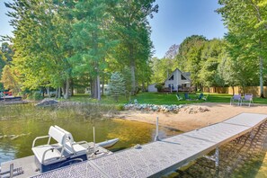 A lakeside property with a dock, a house, and a well-maintained lawn. - Interlochen Lake House w/ Deck, Fire Pit & Dock! (Interlochen)