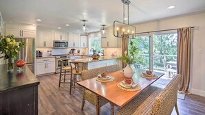 A modern kitchen with white cabinetry, stainless steel appliances, and a wooden dining table set for four. - Chic Lake House w/ Furnished Deck & Hot Tub! (Cedar Glen)
