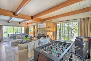 A spacious living room with a foosball table, comfortable seating, large windows, and a stone wall.