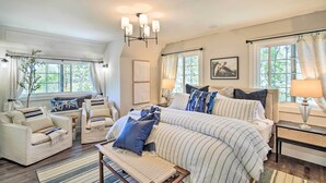 A bedroom with a large bed, two armchairs, a bench, a chandelier, and a window with curtains. - Chic Lake House w/ Furnished Deck & Hot Tub! (Cedar Glen)