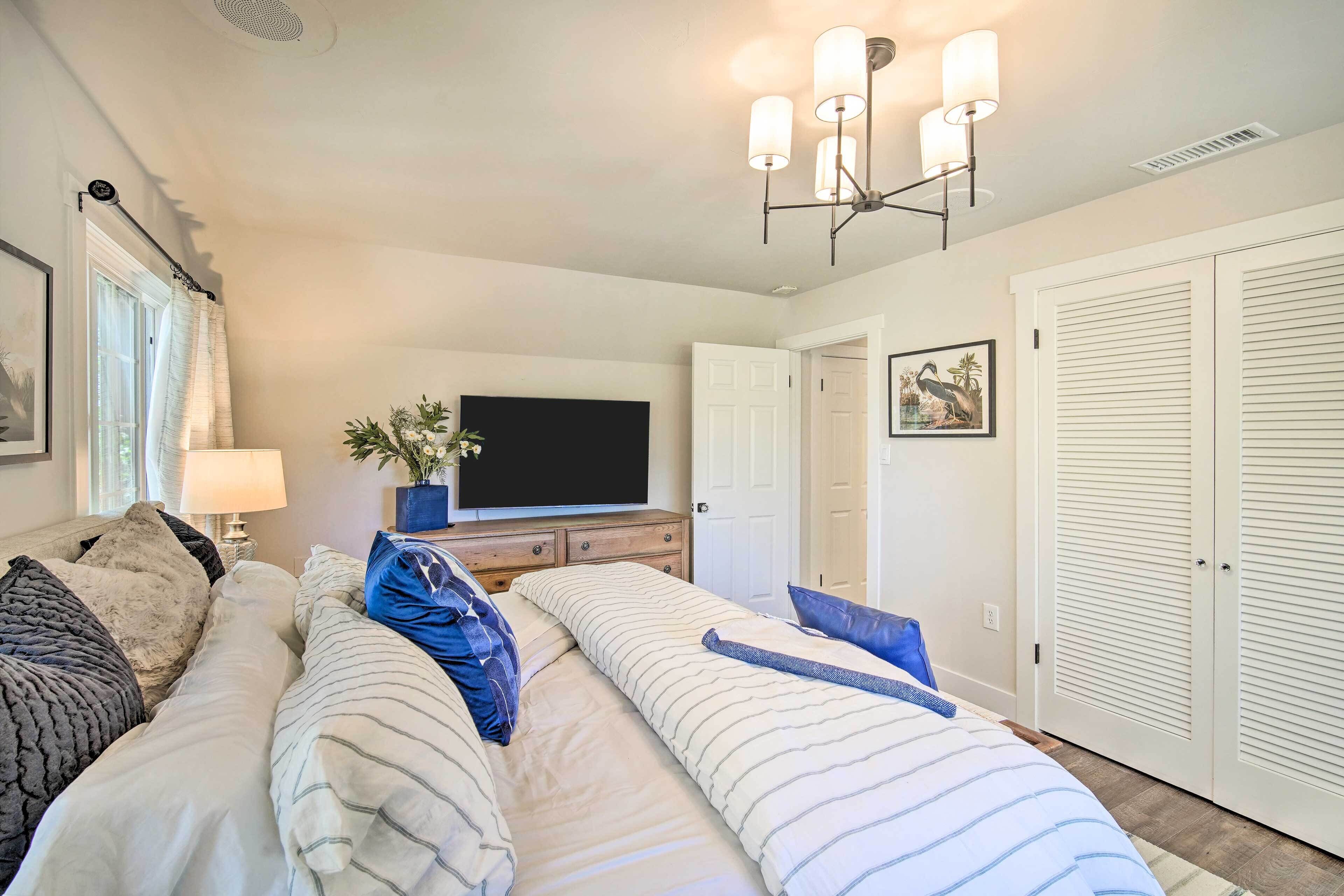 A bedroom with a large bed, a flat-screen TV, a ceiling light fixture, and white closets.
