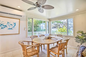 A dining area with a round wooden table and chairs, large windows with a view of greenery, and a ceiling fan.
