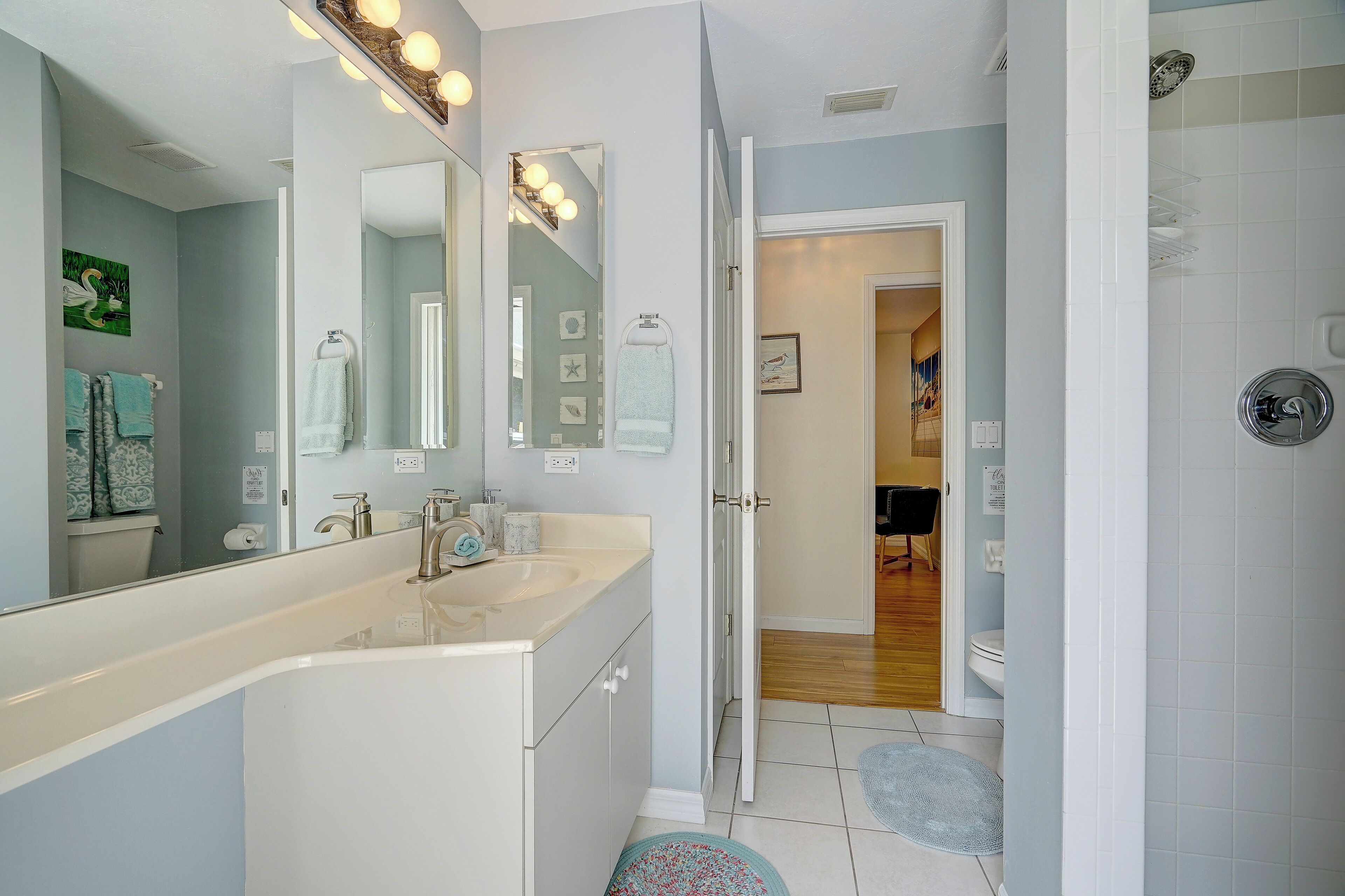 Une salle de bain avec un lavabo blanc, un grand miroir et un espace douche.