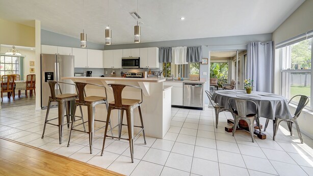 A modern kitchen with a central island, bar stools, and a dining table with chairs. - Game Room & Deck: Spacious Home in St James City (Saint James City)