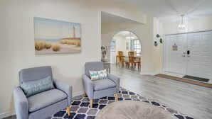 A living room with two grey armchairs, a rug, and a painting of a lighthouse. - Game Room & Deck: Spacious Home in St James City (Saint James City)
