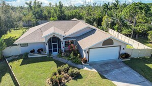 A residential house with a garage, a well-maintained lawn, and a variety of plants and shrubs. - Game Room & Deck: Spacious Home in St James City (Saint James City)