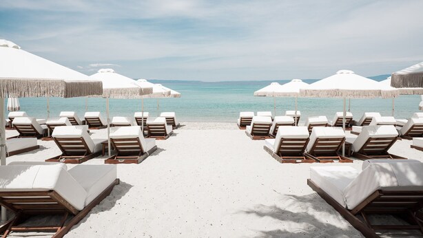 A beach with rows of sun loungers and umbrellas, leading to the water. - Ikyma Boutique (Kassandra)